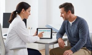 Esta imagen captura el momento de la toma de decisiones compartida entre médico y paciente. Representa una consulta moderna y empática, donde se discuten opciones terapéuticas utilizando herramientas digitales, lo que humaniza el proceso de elección de un tratamiento biológico y la gestión de las expectativas.